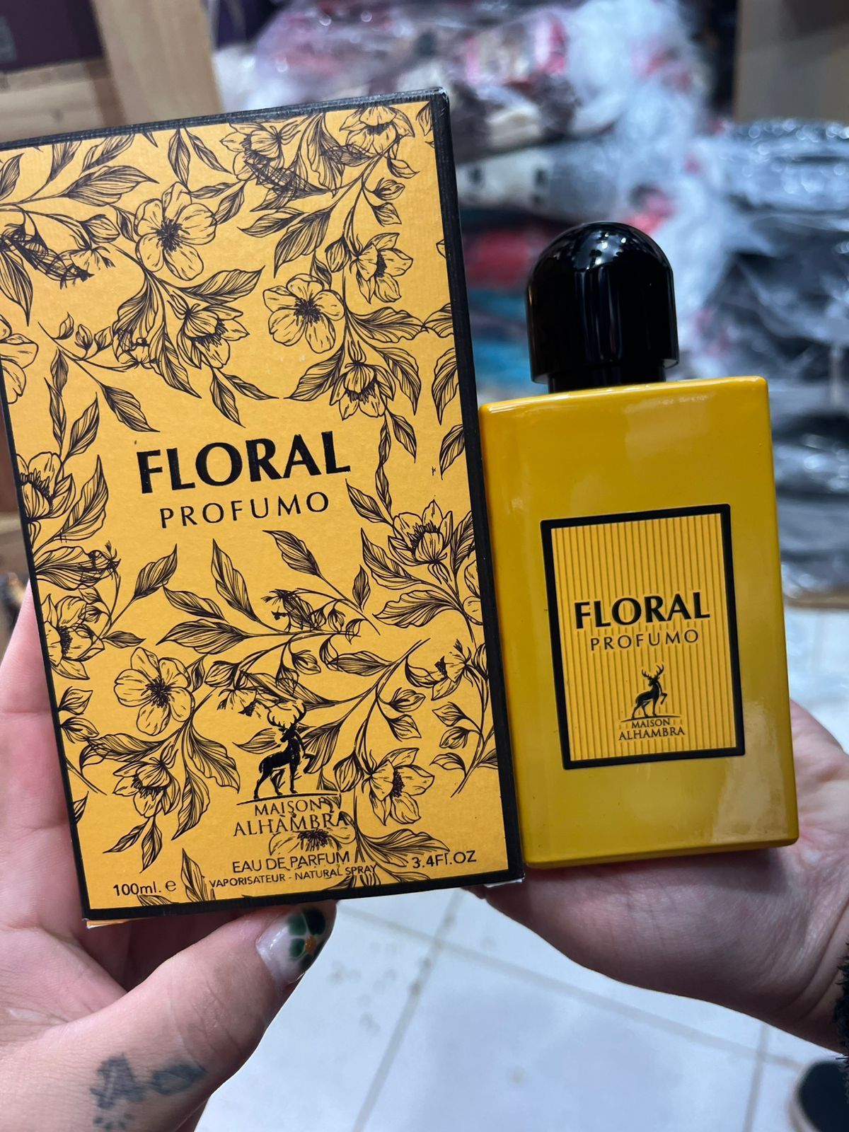 Mano sosteniendo una caja de perfume Floral Profumo amarilla y un frasco a juego con tapón negro.