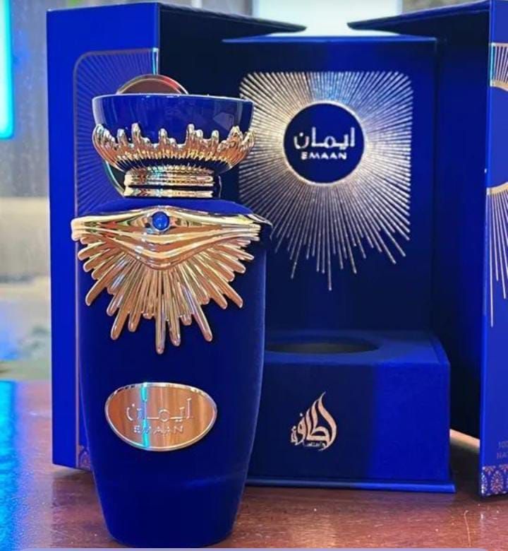 Frasco de perfume azul con corona dorada y detalles de rayos de sol, expuesto frente a un envase azul a juego.