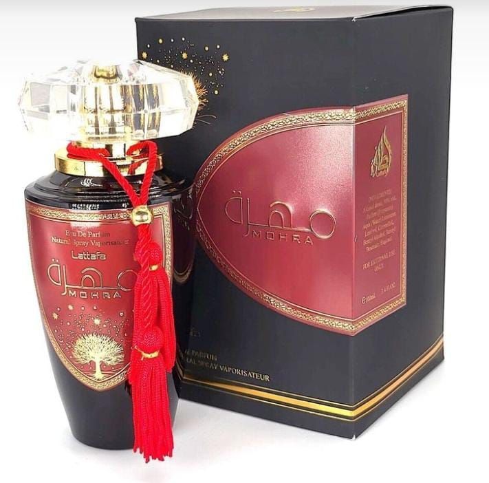 Frasco de perfume con tapón dorado y borla roja junto a una caja de presentación negra y roja.