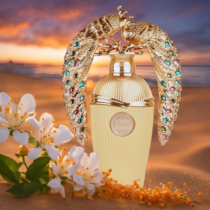 Frasco de perfume de lujo con alas enjoyadas, flores y un fondo de playa al atardecer.