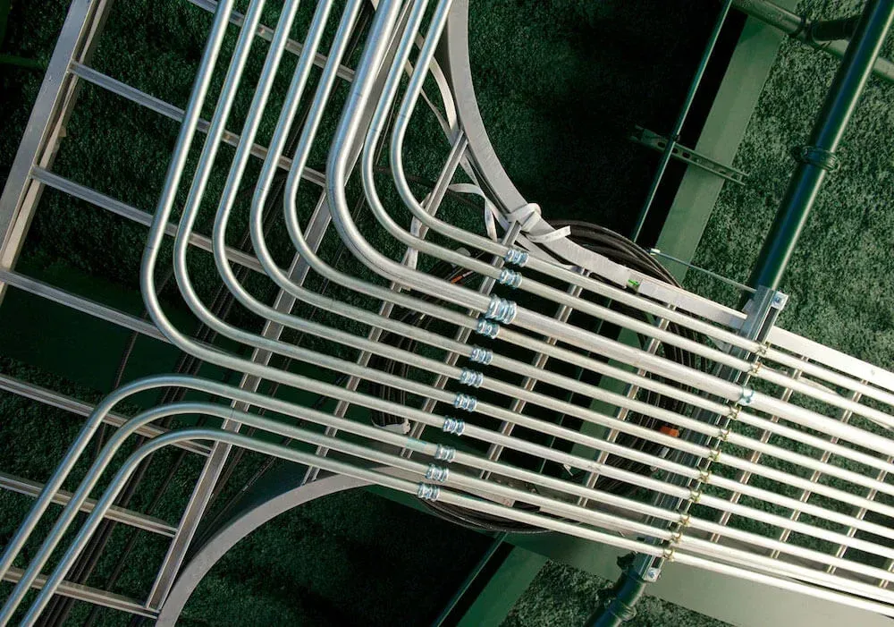Curved white cables crossing over a dark green metal lattice, viewed at an angle.