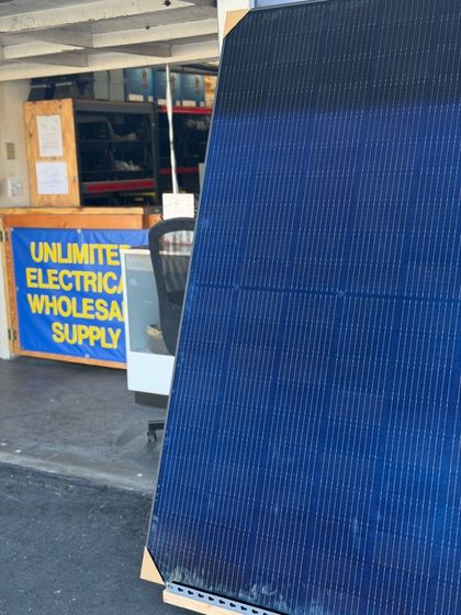 Blue sign reading “Unlimited Electric Wholesale Supply” outside a storefront with a large dark blue tarp or curtain in front.