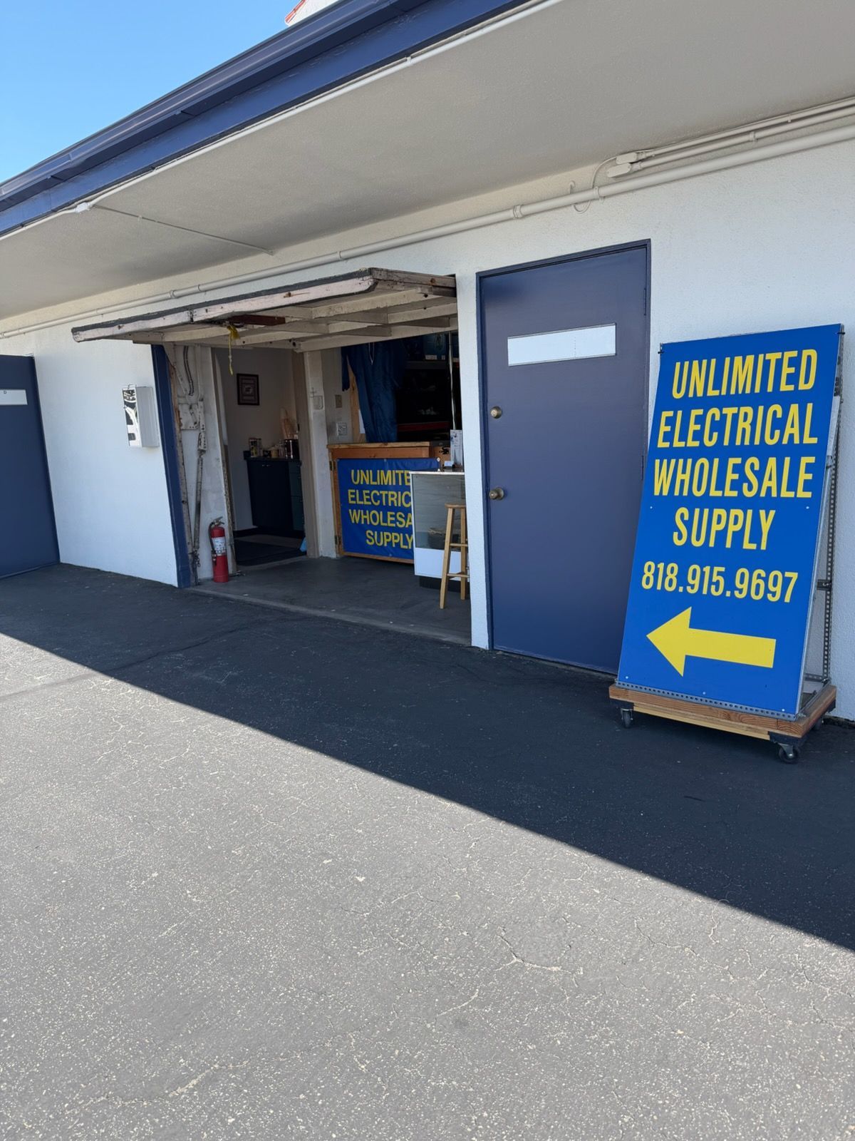 Blue storefront sign for Unlimited Electrical Wholesale Supply at an open warehouse entrance.