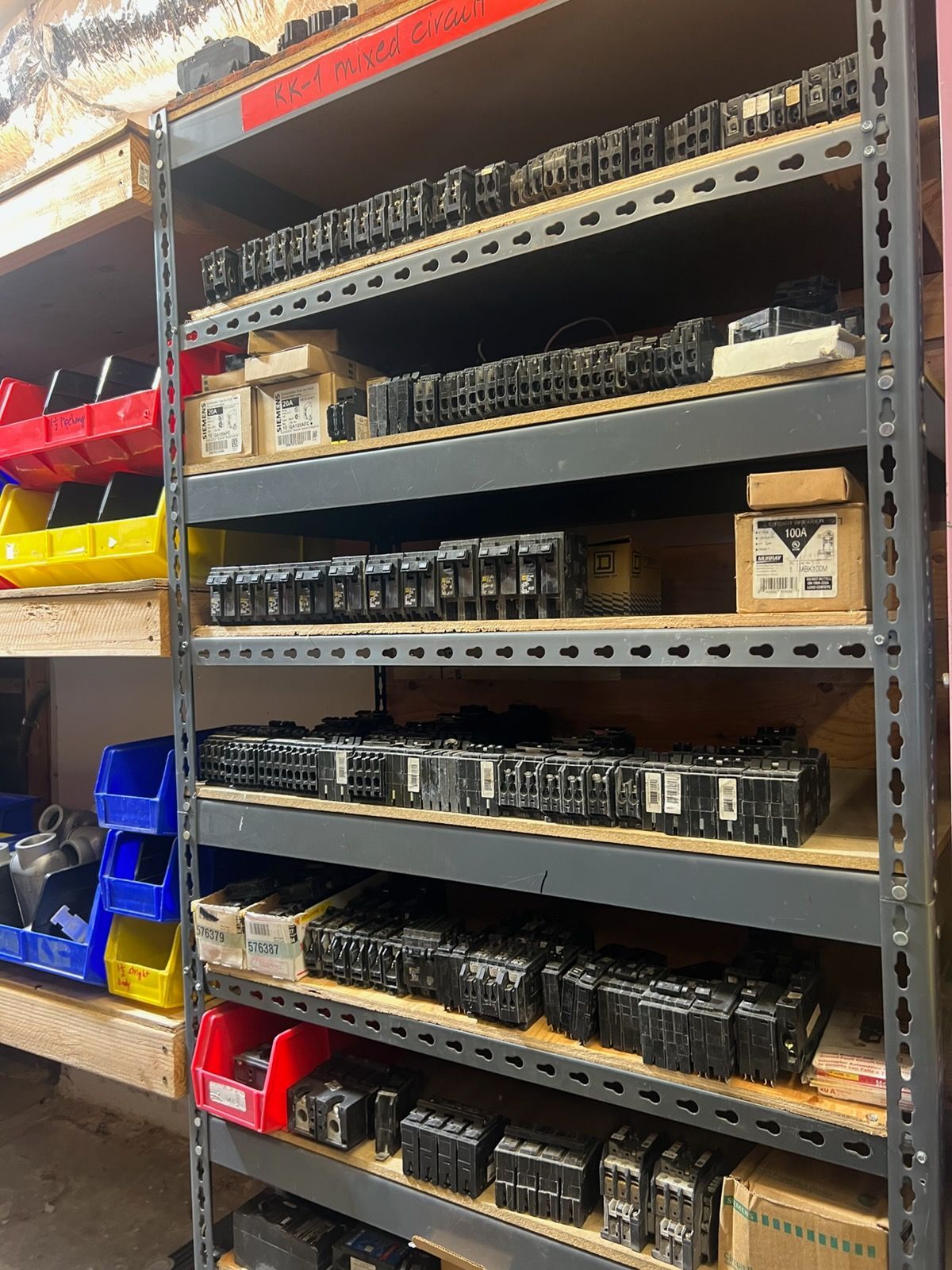 Metal warehouse shelves stocked with rows of small black electronic parts and red, yellow, and blue bins