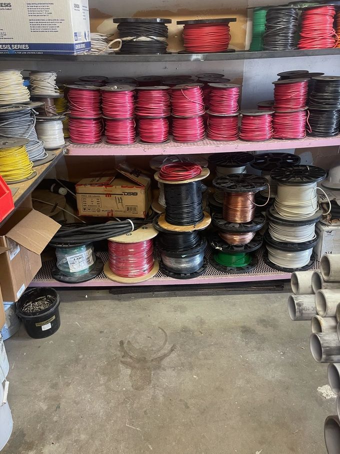 Shelves stocked with coiled wires and cables in red, black, and white in a workshop or store aisle