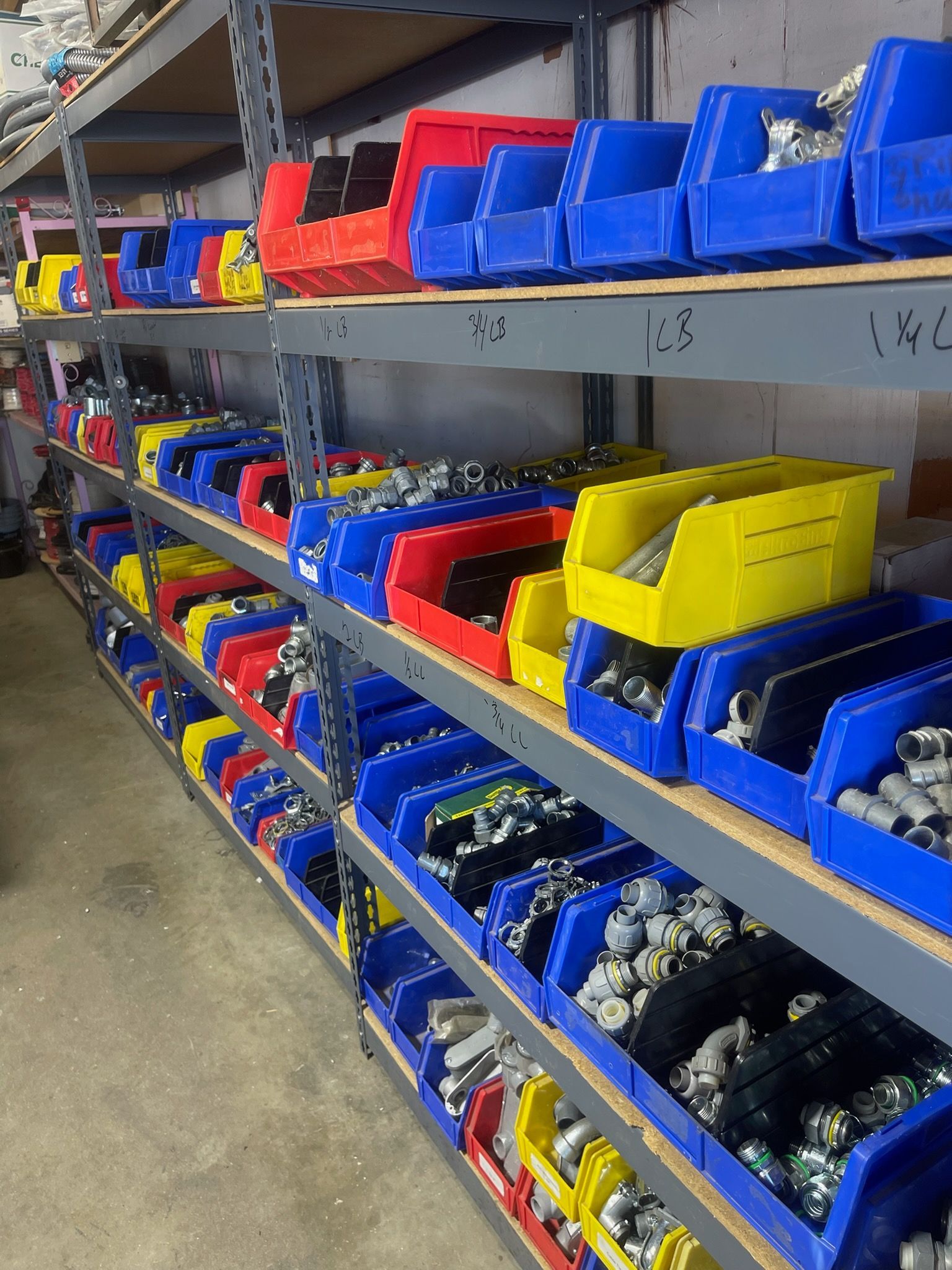 Shelves of blue, red, and yellow plastic bins holding small parts in a workshop or warehouse.