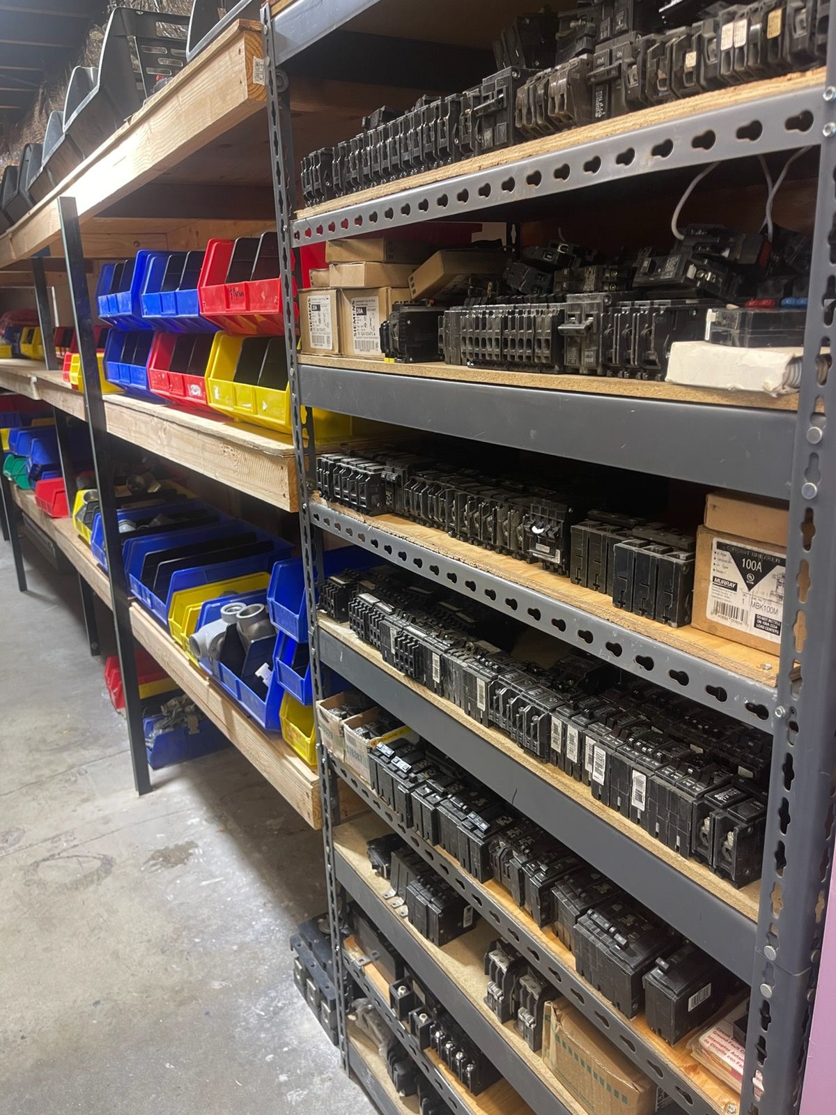 Warehouse aisle with metal shelves stocked with labeled plastic bins and containers.