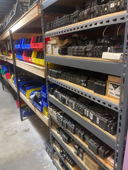 Warehouse aisle with metal shelves stocked with labeled plastic bins and containers.