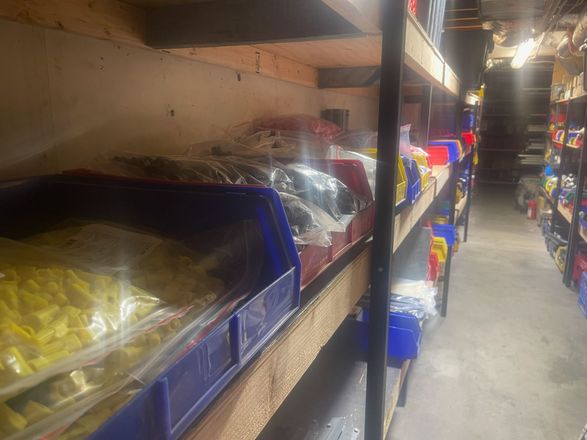 A storage aisle with shelves of packed goods in plastic bins and bags under dim lighting.