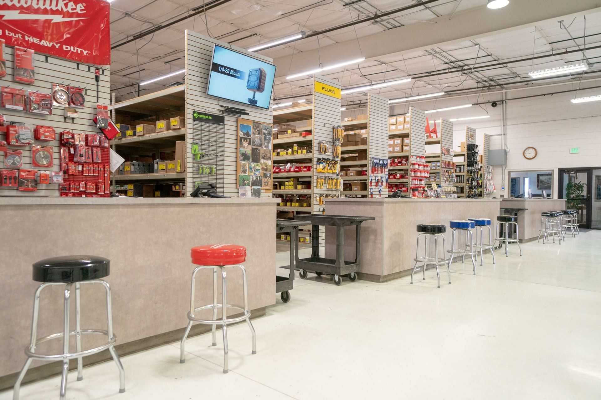 Bright retail store interior with shelves, checkout counter, stools, and a wall-mounted TV.