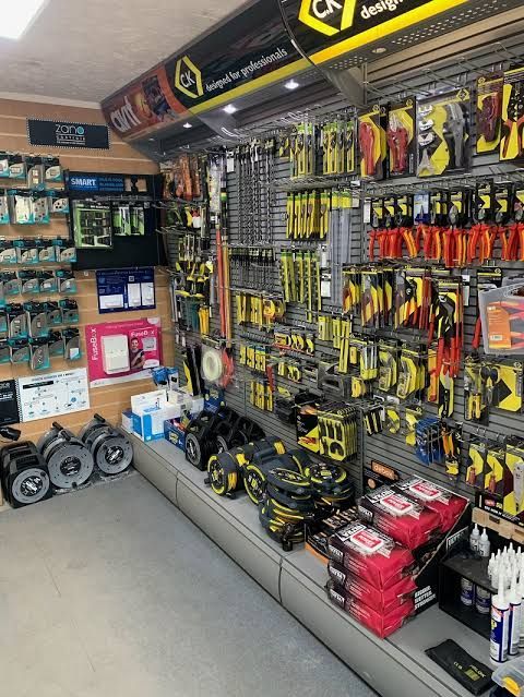 Hardware store aisle with hanging tools and accessories, neatly stocked shelves, and boxed items on the floor.