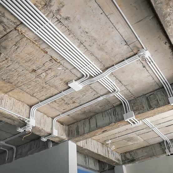 Concrete ceiling with exposed white electrical conduit and wiring in an unfinished interior space