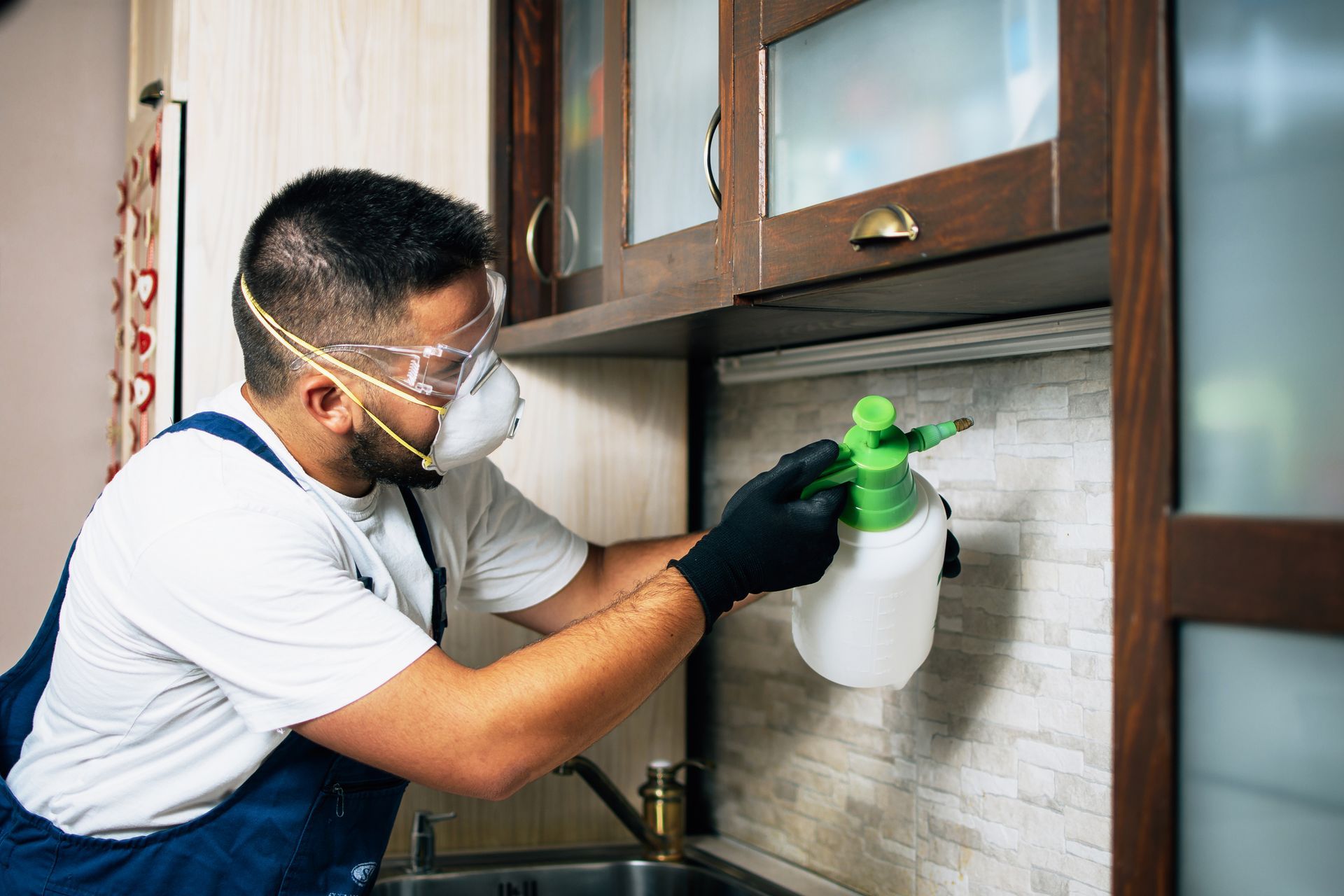 A professional exterminator is spraying pesticide in a kitchen.