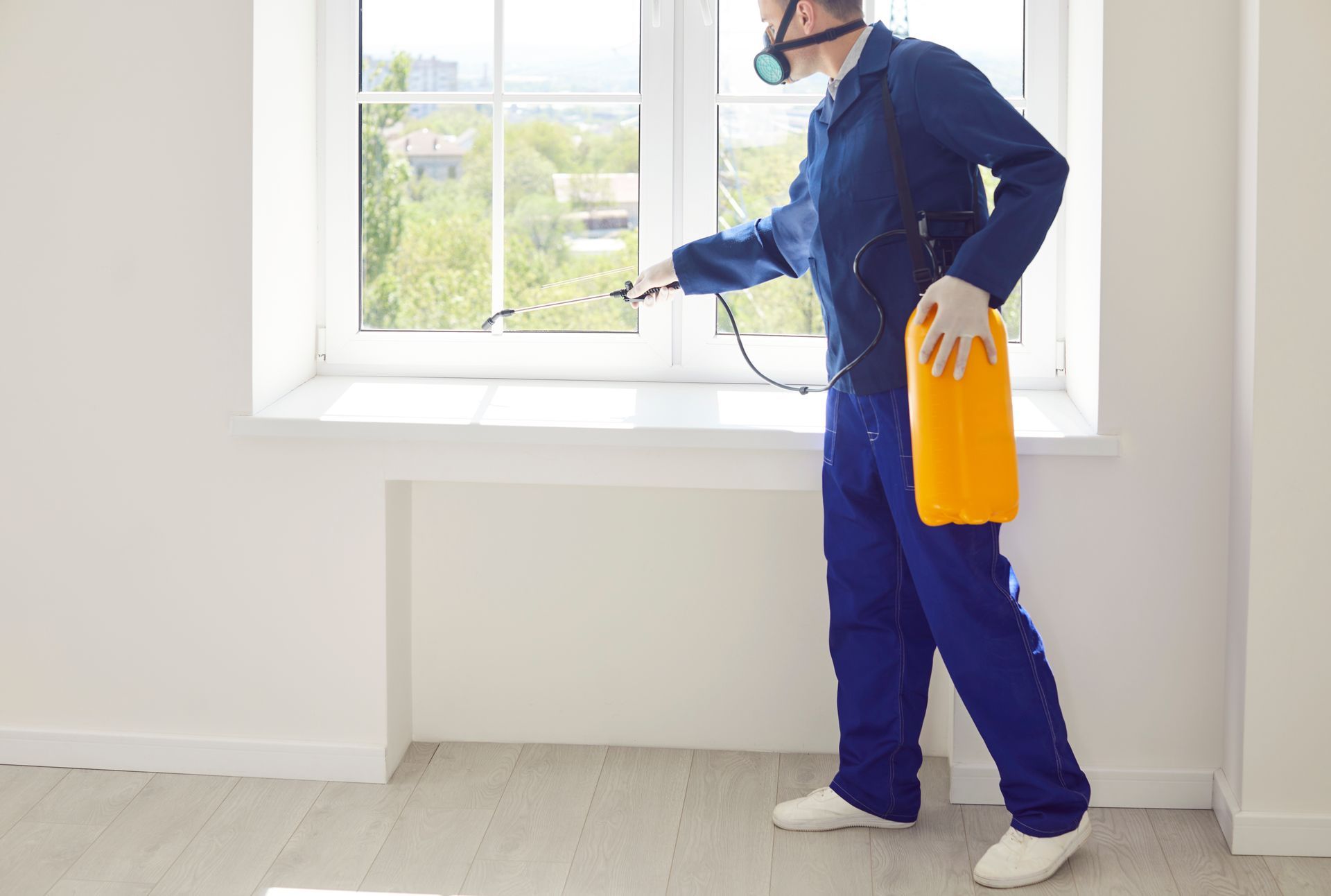 A technician from a termite company wearing a mask and spraying a windowsill for pest control.