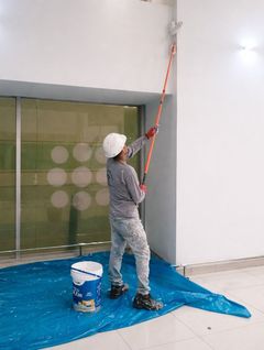 Un obrero de la construcción, con chaleco reflectante y casco, utiliza un rodillo para aplicar una capa impermeabilizante azul a un pilar.