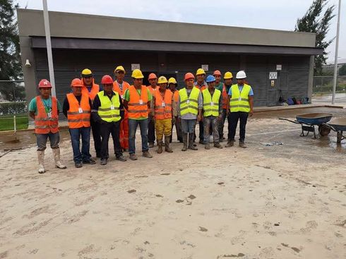 Técnico con uniforme de trabajo y guantes inspeccionando cilindros de gas industrial plateados conectados a tuberías rojas aéreas.