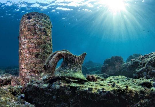 Underwater ruins with a curved stone arch and a sunlit column on the seabed