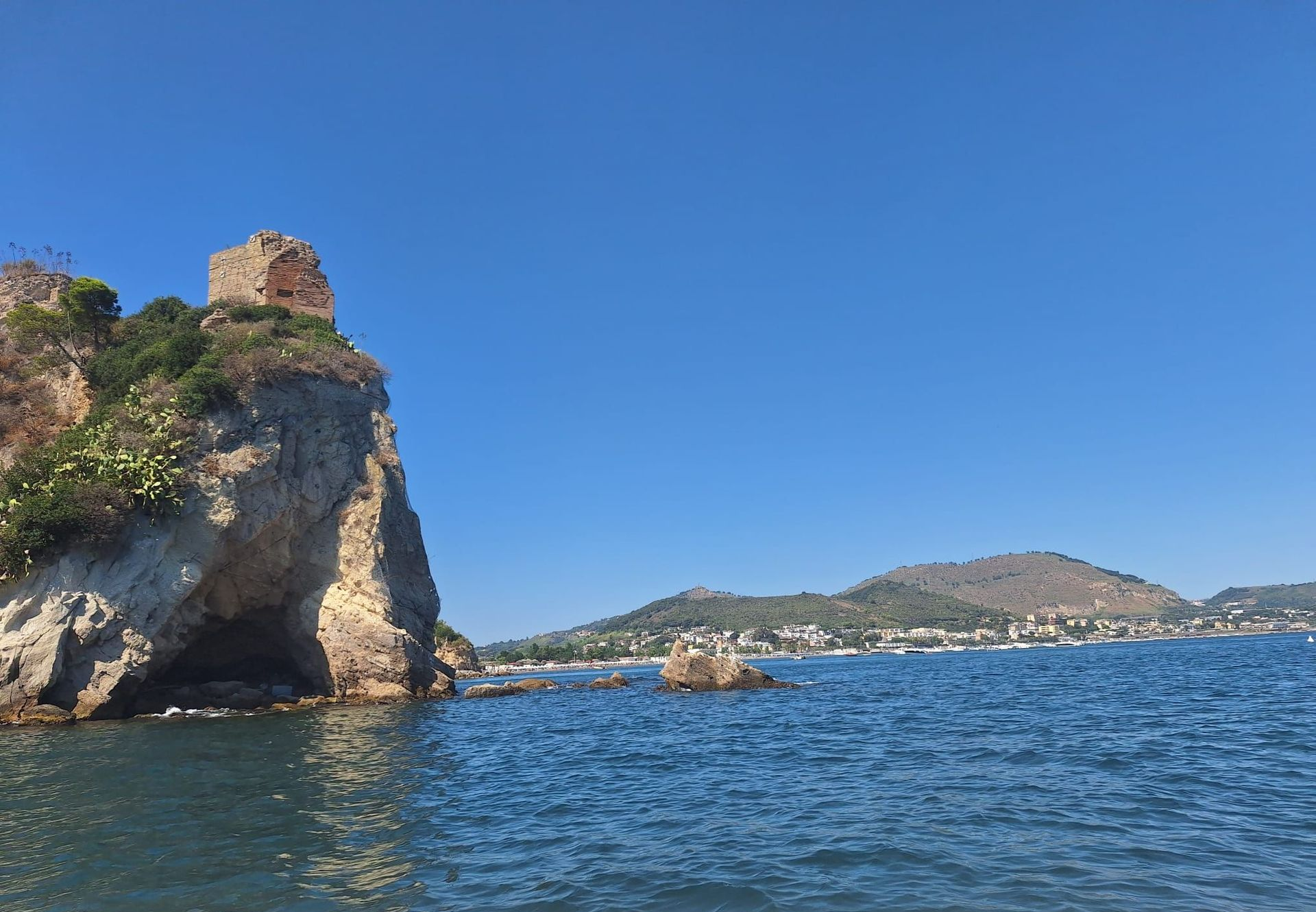 Rocky seaside cliff with old stone ruins above blue water under a clear sky