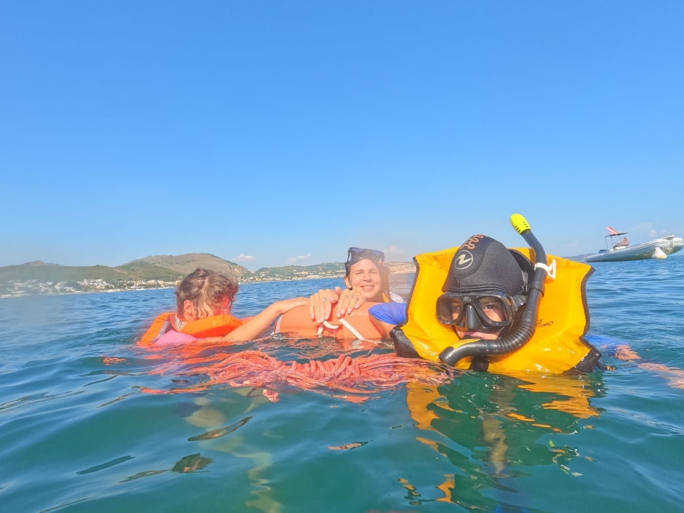 Three snorkelers floating in blue water, one in yellow gear, with a coastline in the distance