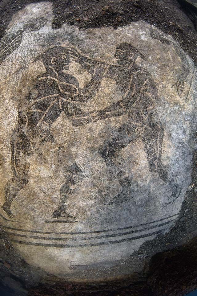 Ancient rock carving of a standing figure with raised arms, weathered and faded on a dark stone surface