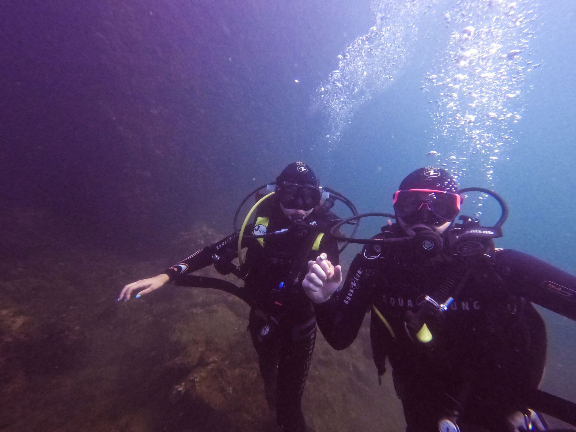Two scuba divers underwater, one giving a thumbs-up in blue light