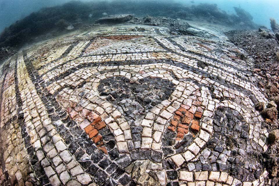 Underwater mosaic floor with circular patterns and fish-like designs in muted beige, orange, and gray tones