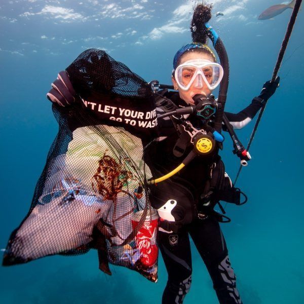 Scuba diver underwater holding a large net bag of collected trash, wearing mask and snorkel
