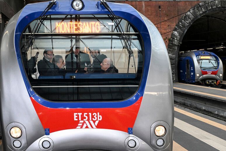 Front view of a modern gray, blue, and red subway train at a station platform, with passengers inside.