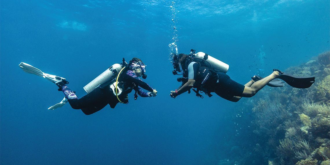 Two scuba divers swimming underwater near a coral reef