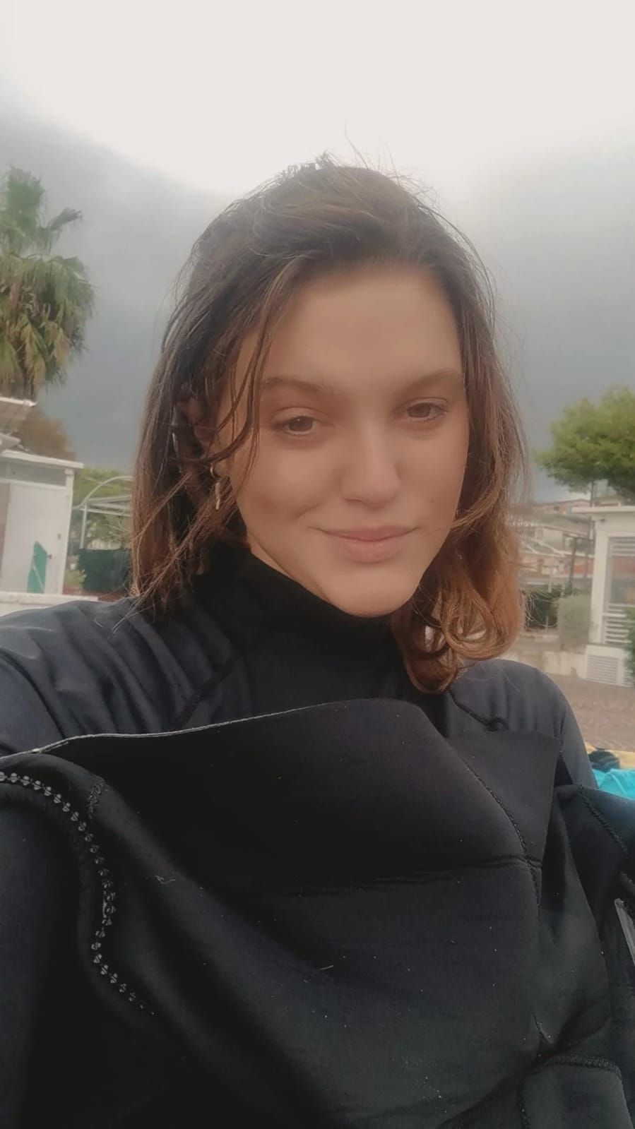 Person in a black top smiling outdoors with mountains and cloudy sky in the background