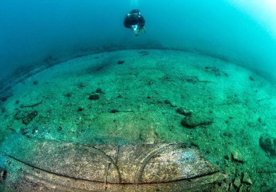 Underwater view of a large green dome-like structure on the seafloor with a diver above