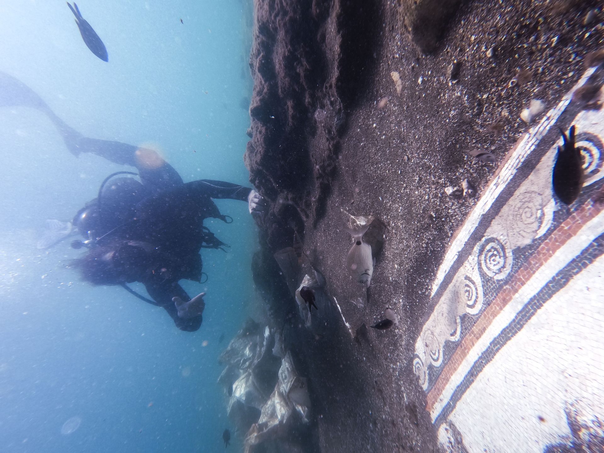 Scuba diver swimming beside a boat hull underwater, with blue water and visible hull markings