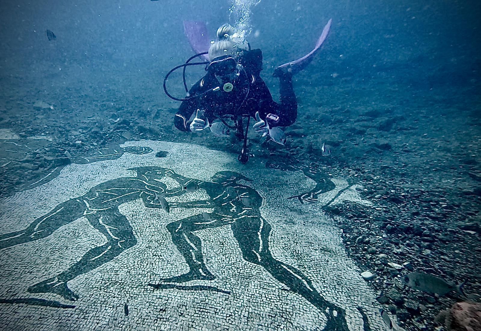Scuba diver hovering over an underwater mosaic of a human figure on the seafloor