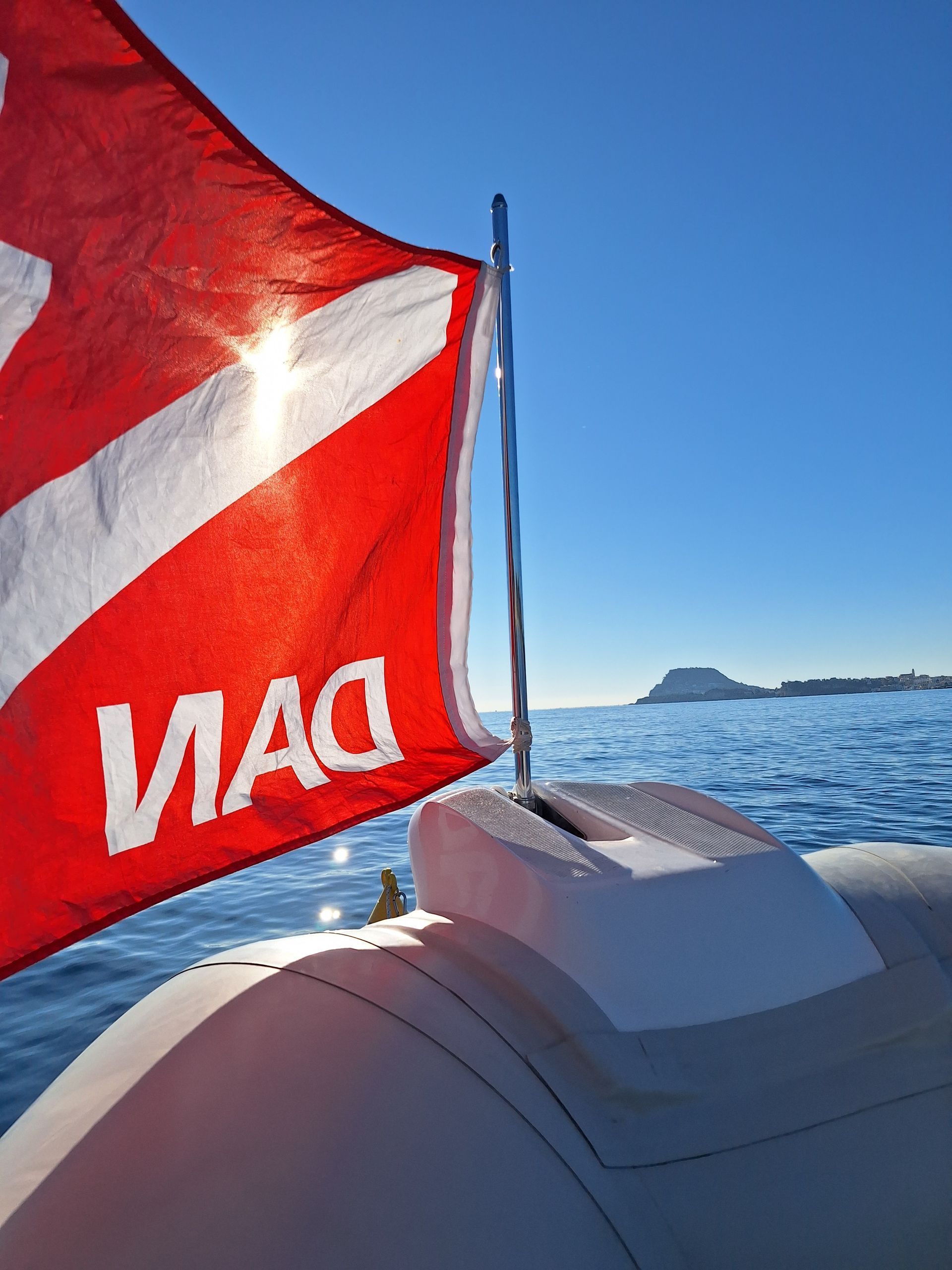 Red DAN flag on a boat with ocean and a distant island under a clear blue sky