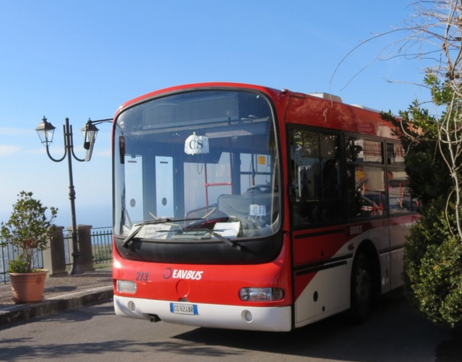 Red and white bus parked by the seaside with street lamps and greenery nearby