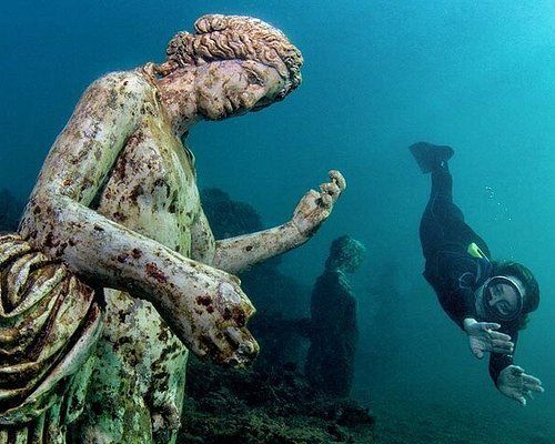 Underwater statue beside scuba divers exploring a submerged scene