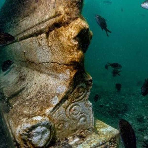 Ancient stone statue underwater with small fish swimming nearby