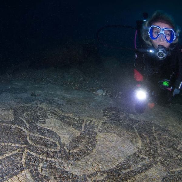 Diver with blue mask and flashlight exploring a dark underwater site with a carved rock formation