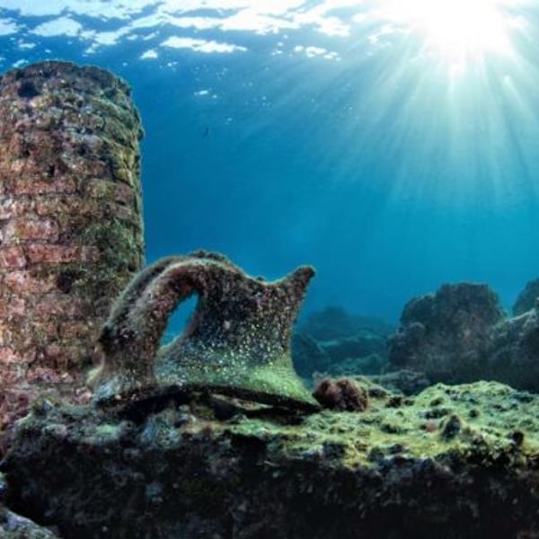Sunlit underwater coral reef with a large rock formation and blue ocean background