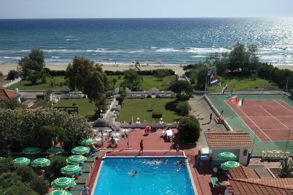 Resort pool and tennis court overlooking a sunny ocean shoreline