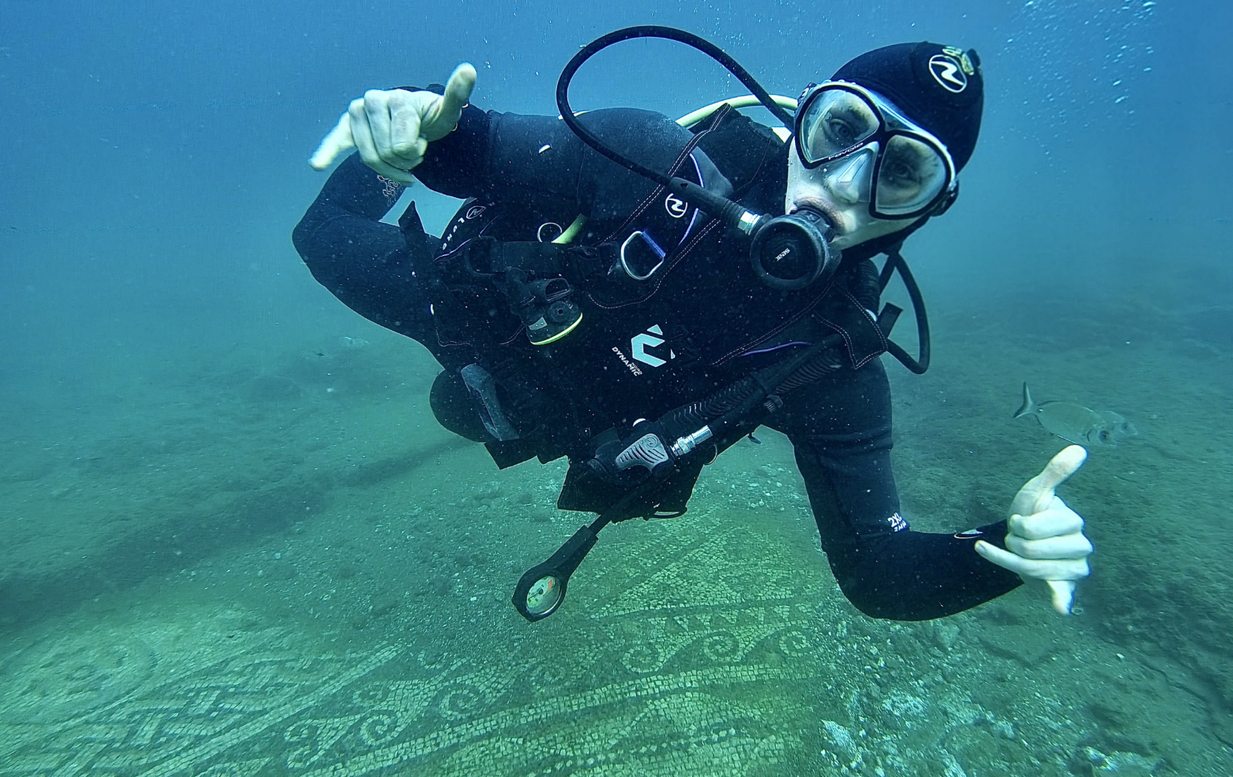 Scuba diver underwater giving a thumbs-up over a green seafloor mosaic