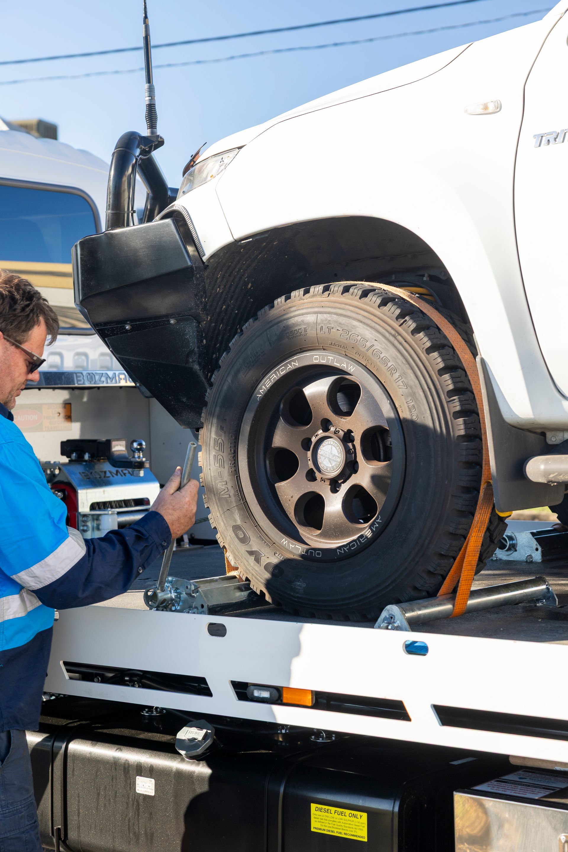 Tow truck operator securing a white truck with an orange strap. Sunny outdoor setting.— Perlyn Towing in Emerald, QLD