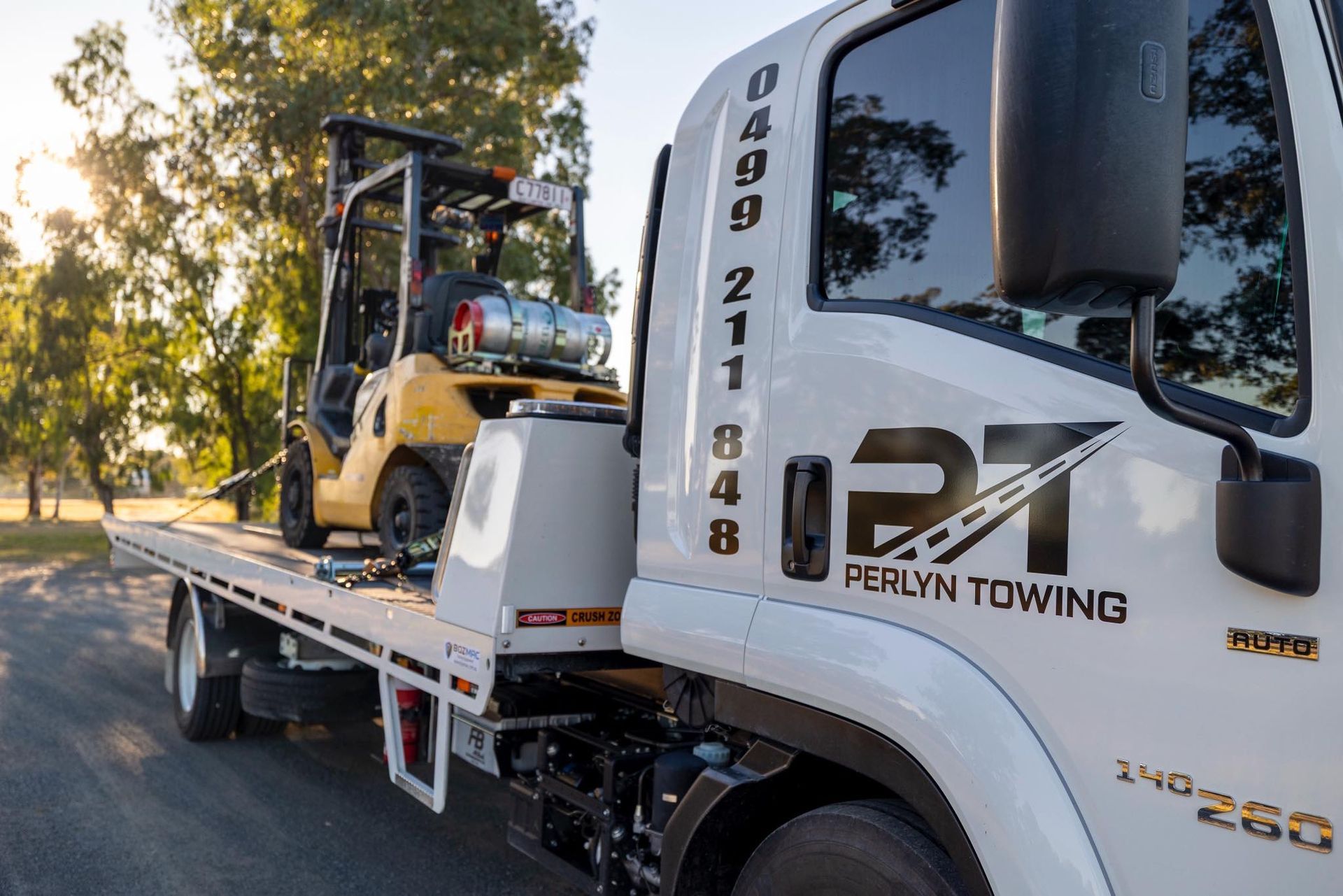 A flatbed tow truck carrying a yellow forklift. Ferlyn Towing logo is visible.— Perlyn Towing in Emerald, QLD