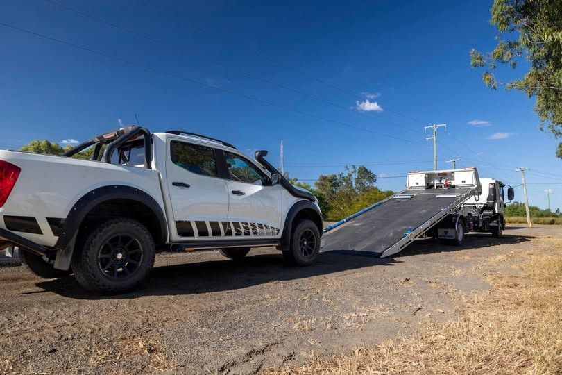 White pickup truck being towed by a flatbed tow truck on a dirt road under a blue sky.— Perlyn Towing  in Gladstone, QLD