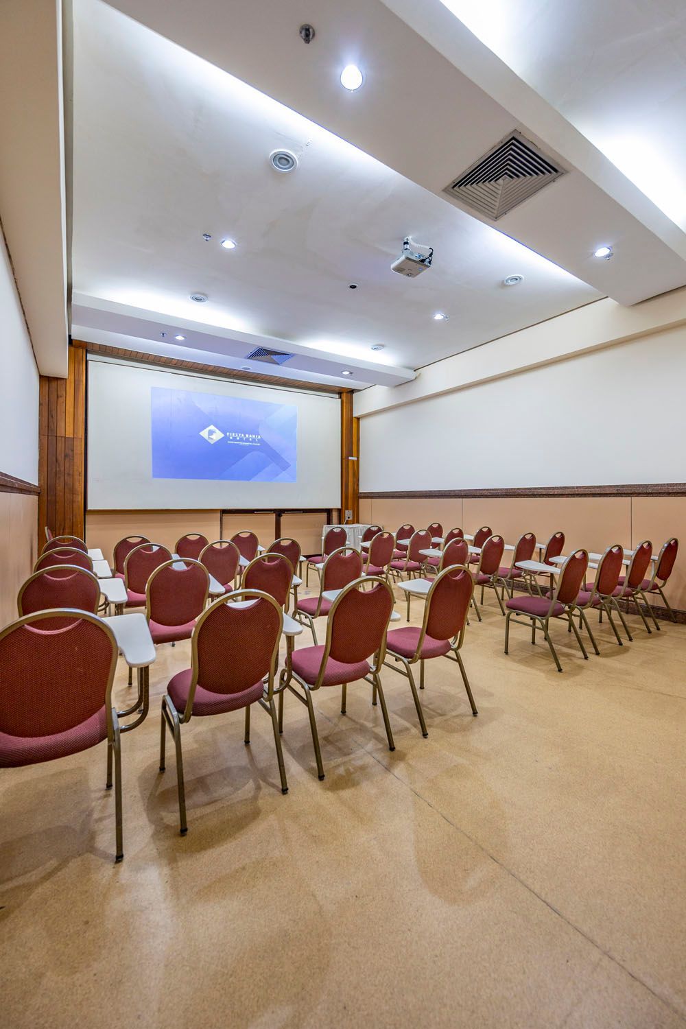 Uma grande sala de conferências com mesas e cadeiras e uma tela de projetor.