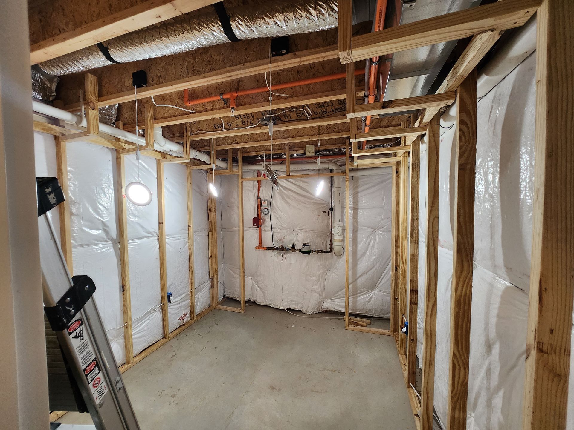 Unfinished basement with exposed wooden framing, insulation, concrete floor, and a ladder on the left.