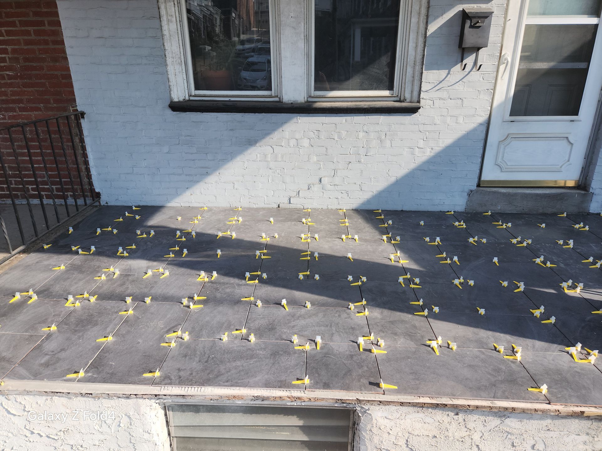 Dark tiles on a porch with yellow leveling clips, door on right, window above.