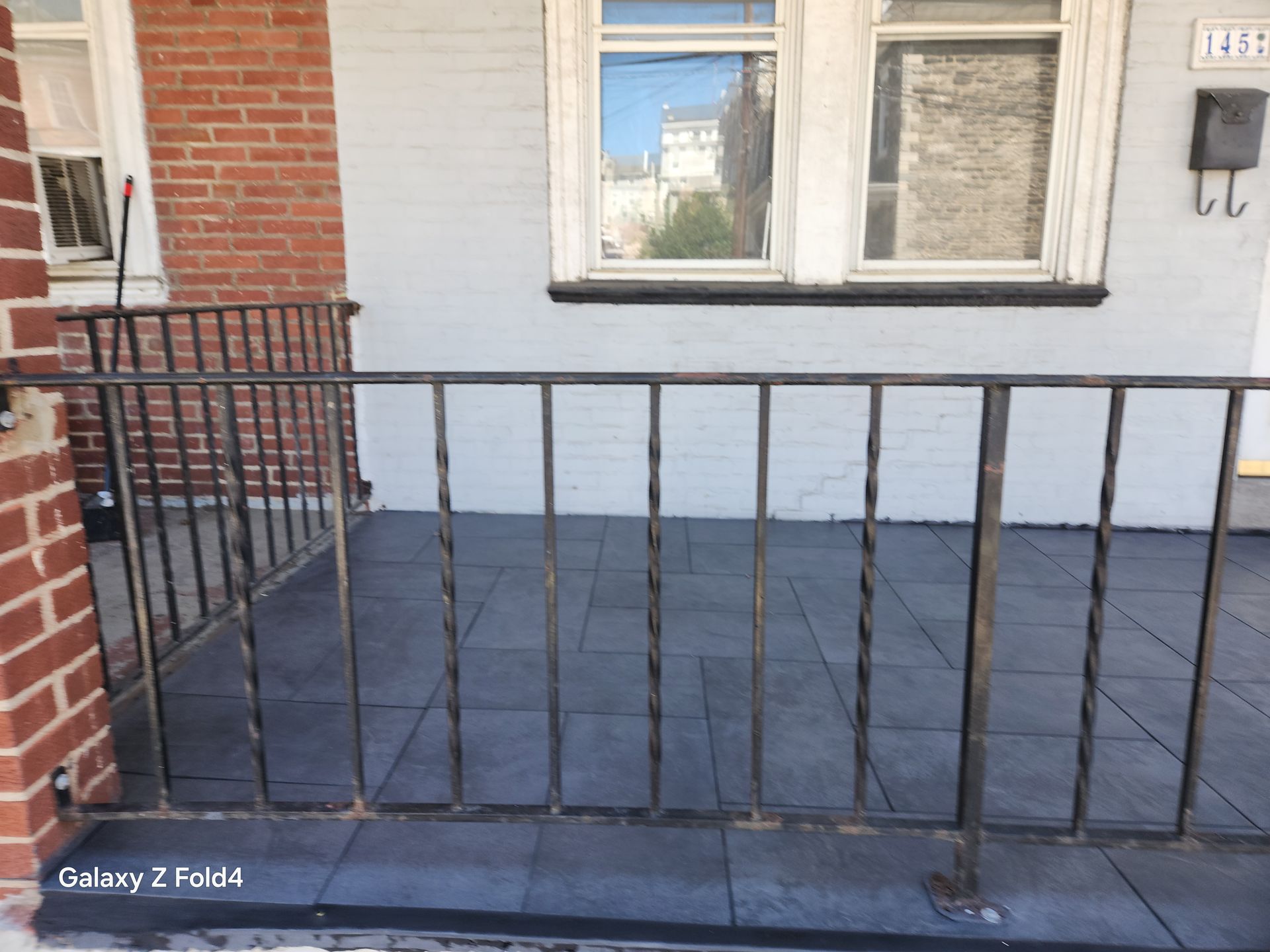 Black iron railing on a porch with gray tiles and a white-framed window.