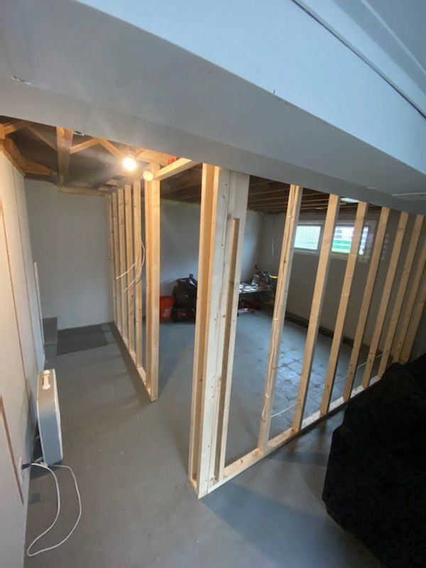 Basement room under construction, with wooden frame walls, exposed wiring, and concrete floor.