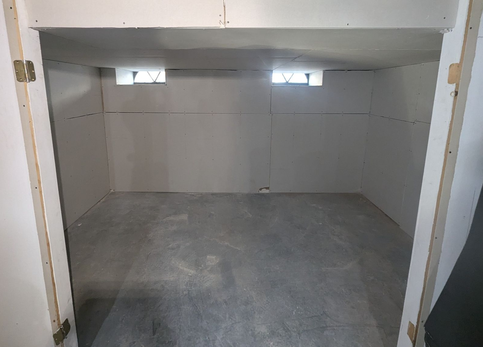 Empty concrete storage alcove with small high windows and white walls